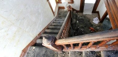 The image shows a damaged wooden staircase with broken or missing steps, exposed structural beams, and debris scattered on the floor below.RetryClaude can make mistakes. Please double-check responses.